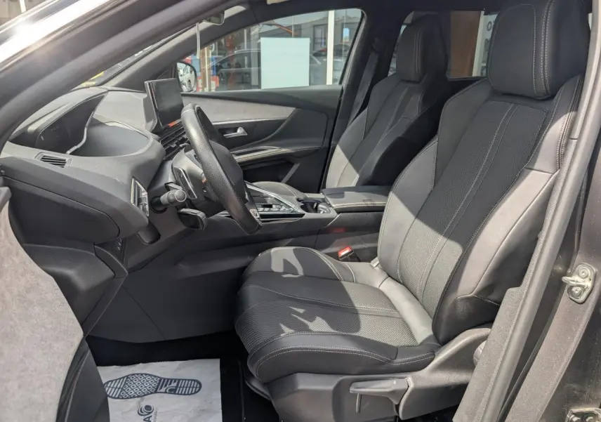 Vue intérieure côté conducteur du Peugeot 5008 gris 2023, mettant en valeur les sièges avant en cuir et le tableau de bord moderne.