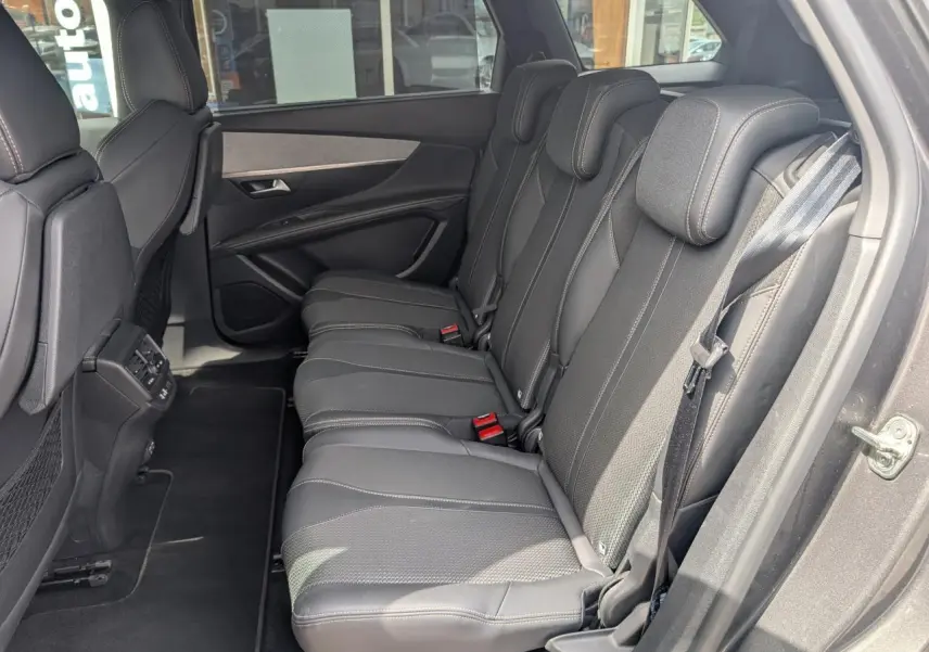 Vue côté droit des trois sièges arrière noirs du Peugeot 5008 2023, avec ceintures et panneaux de porte gris foncé.