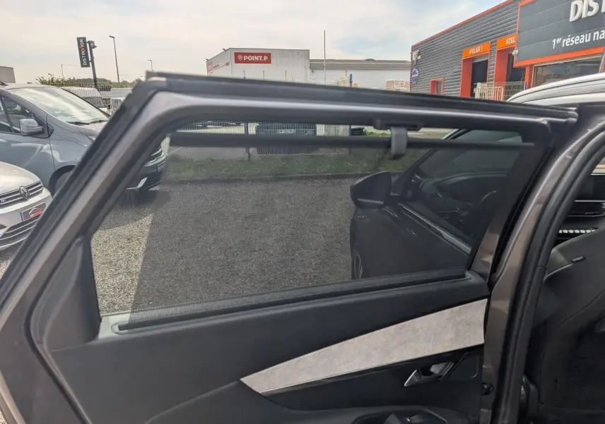 Vue intérieure côté gauche de la porte arrière ouverte d’un Peugeot 5008 gris 2023 avec vitrage surteinté et habillage Alcantara.