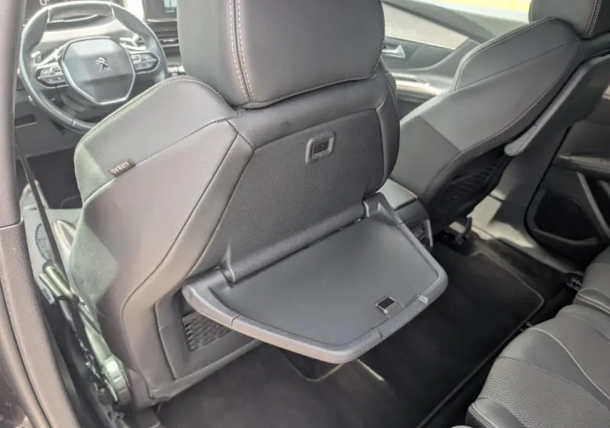 Vue intérieure arrière montrant le dossier du siège avant gauche gris avec tablette rabattable déployée sur un Peugeot 5008 GT 2023.