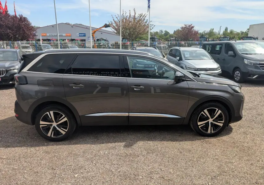 Profil droit d’un Peugeot 5008 gris métallisé 2023 GT avec jantes alliage bi-ton et vitres arrière surteintées.