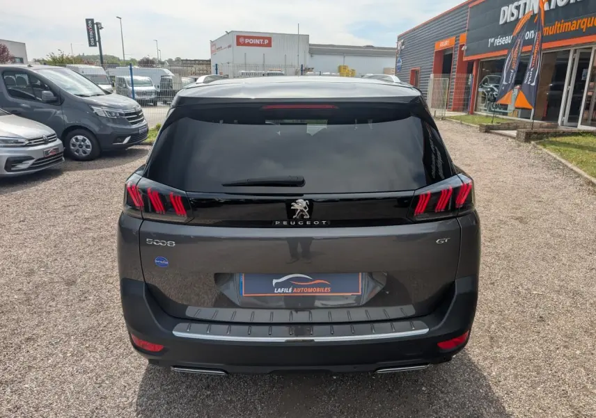 Vue arrière d'un Peugeot 5008 gris métallisé 2023 GT avec feux LED 3D et hayon mains libres sur parking.