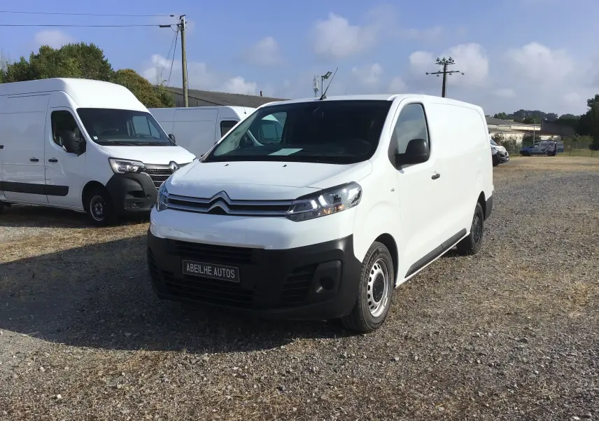 Vue 3/4 avant d’un Citroën Jumpy blanc 2021 avec pare-chocs noir et jantes acier sur un terrain gravillonné.