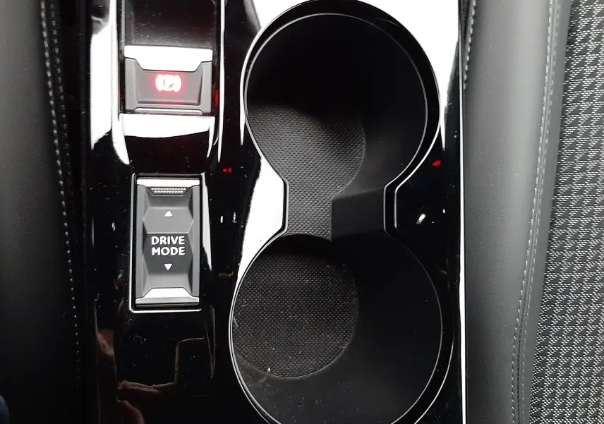 Gros plan sur la console centrale noire brillante du Peugeot 2008 2023 avec porte-gobelets et bouton Drive Mode.