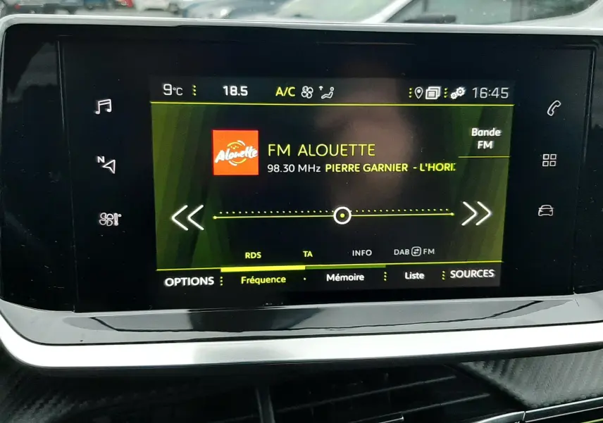 Écran tactile central du Peugeot 2008 2023 affichant la radio FM Alouette, avec tableau de bord noir et extérieur flou.