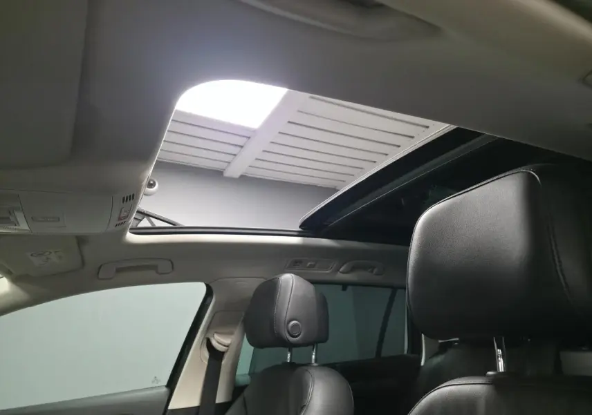 Vue intérieure du toit ouvrant panoramique ouvert et des sièges avant en cuir noir d'une Volkswagen Passat SW gris.