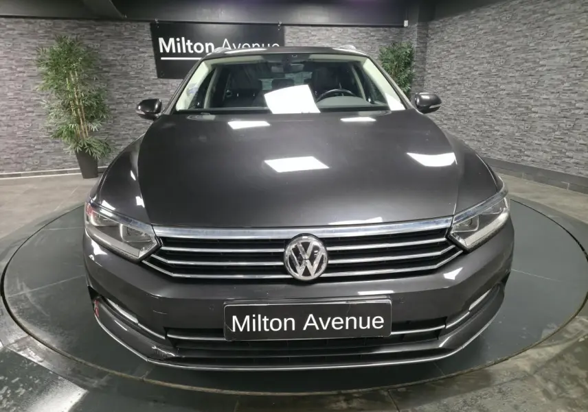 Vue frontale d'une Volkswagen Passat SW gris métallisé avec calandre chromée et logo VW visible en showroom.