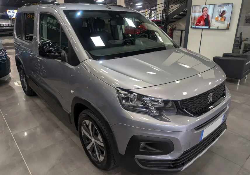 Peugeot Rifter gris Artense en 3/4 avant droit, avec calandre noire et jantes alliage bicolores visibles en showroom.