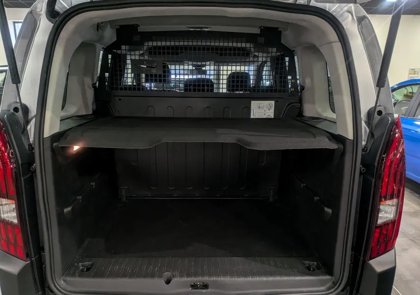 Coffre ouvert vu de l’arrière d’un Peugeot Rifter gris Artense 2024 avec séparation grillagée et tablette de rangement.