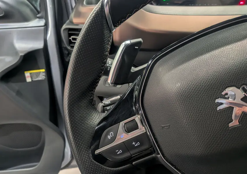 Gros plan sur le volant en cuir noir du Peugeot Rifter 2024, mettant en valeur les commandes intégrées côté gauche.