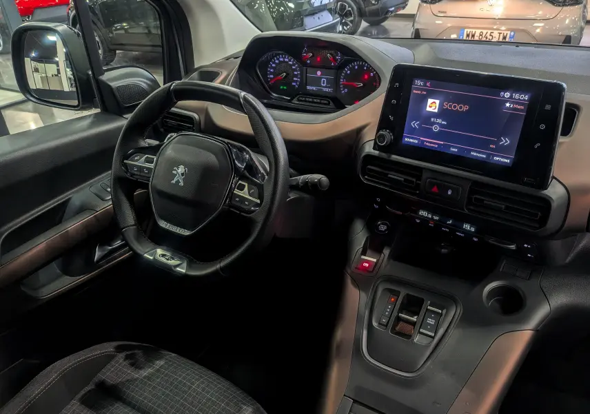 Vue intérieure du poste de conduite du Peugeot Rifter 2024, avec volant multifonction, tableau de bord digital et écran tactile central.