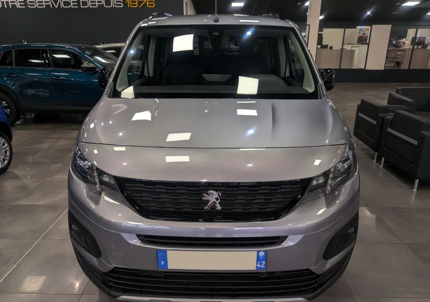 Vue frontale d'un Peugeot Rifter 2024 gris Artense en showroom, avec calandre noire et logo lion central visible.