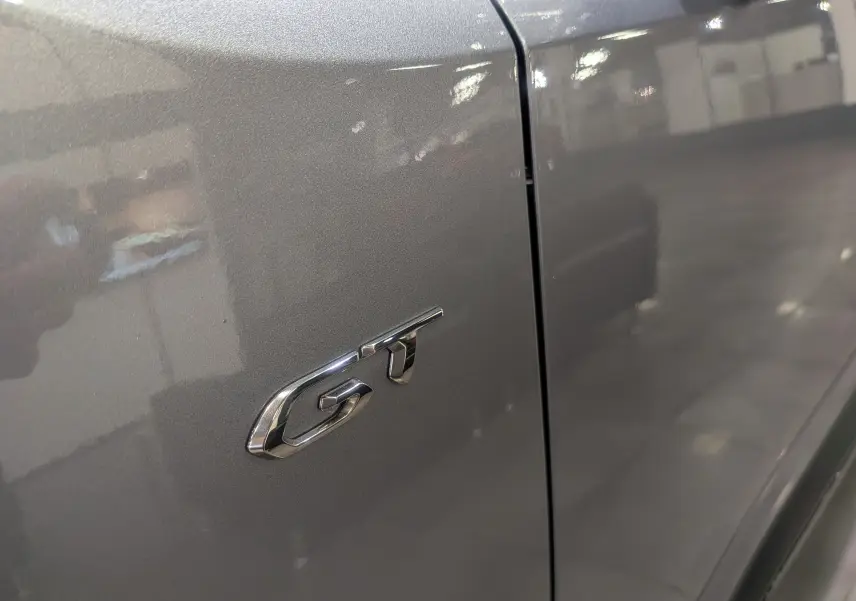 Gros plan sur l’inscription GT en chrome sur la porte gris Artense d’un Peugeot Rifter 2024.