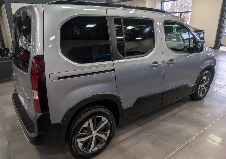 Vue 3/4 arrière droite du Peugeot Rifter 2024 gris Artense avec jantes alliage et vitres teintées en showroom.