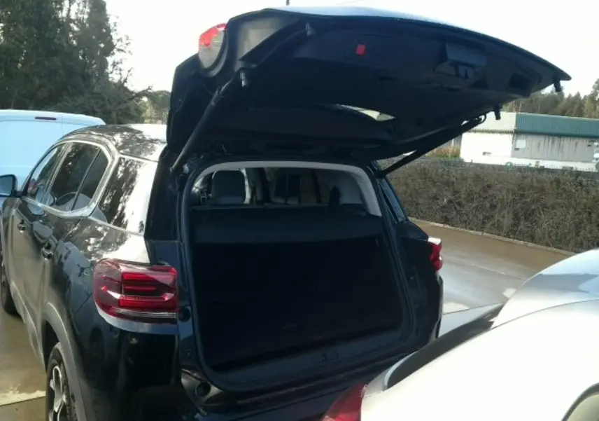 Vue arrière 3/4 gauche du Citroën C5 Aircross noir Perla avec hayon électrique ouvert montrant le coffre vide.