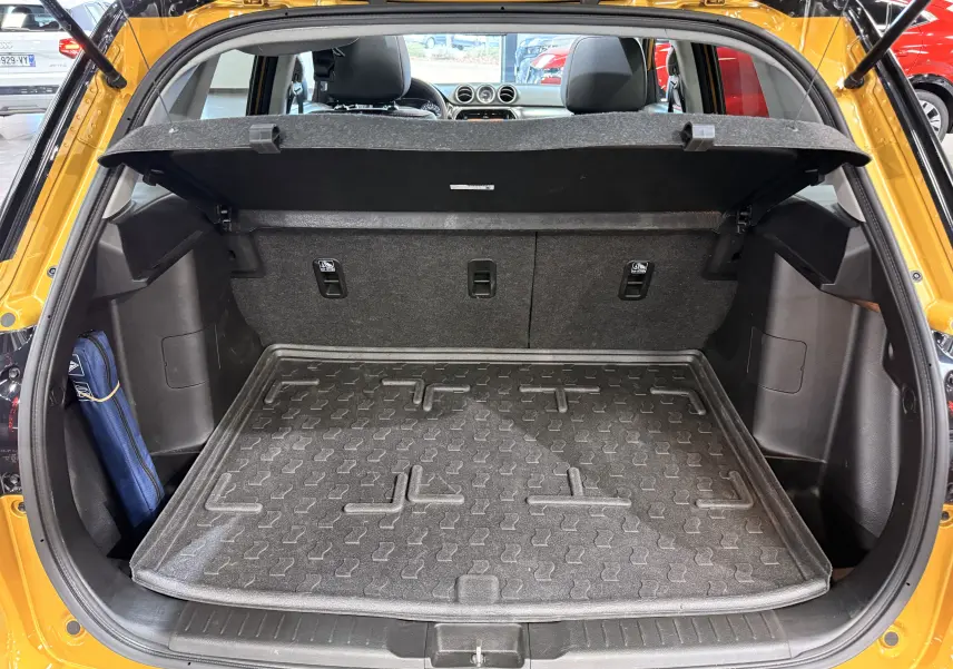 Coffre ouvert vu de l'arrière d'un Suzuki Vitara 2023 jaune toit noir, avec tapis de protection et banquette arrière visible.