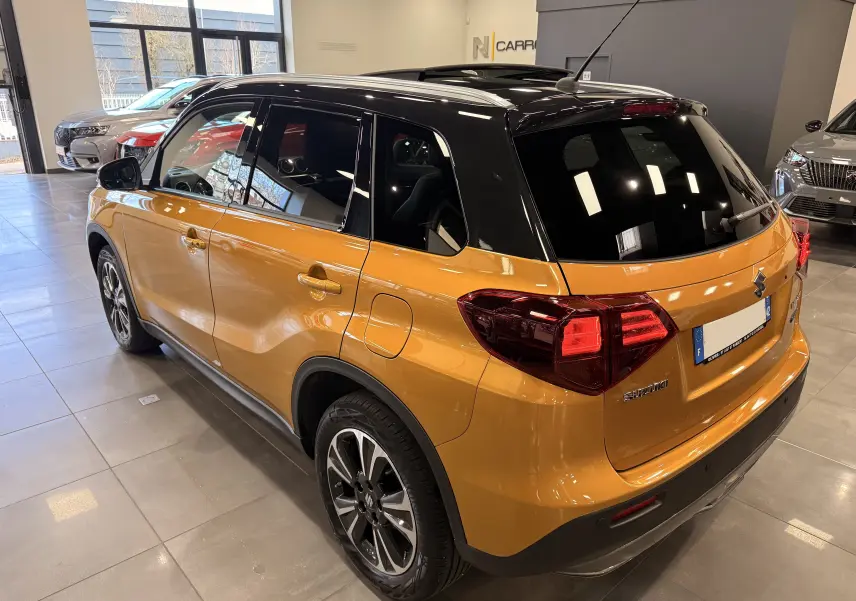 Vue 3/4 arrière droite du Suzuki Vitara 1.5 Dualjet Hybrid 2023 jaune avec toit noir brillant en showroom.