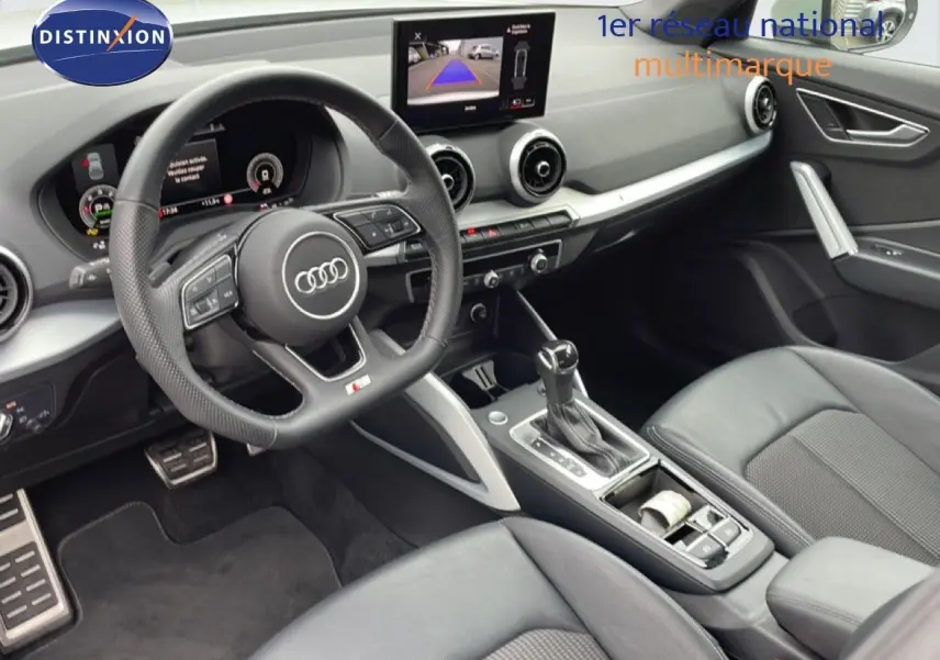 Vue intérieure côté conducteur de l'Audi Q2 2025, avec volant cuir, console centrale et écran multimédia affichant la caméra de recul.