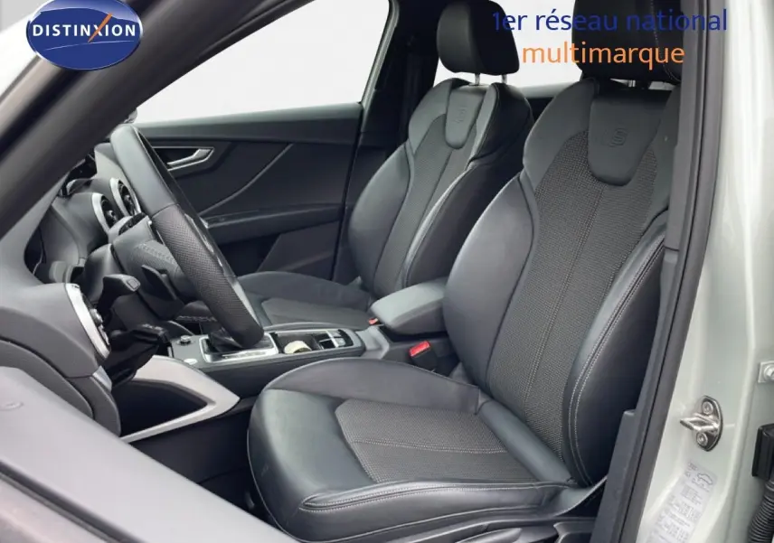 Vue intérieure côté conducteur de l'Audi Q2 argent rose métal 2025, sièges sport cuir noir avec logo S-Line embossé.