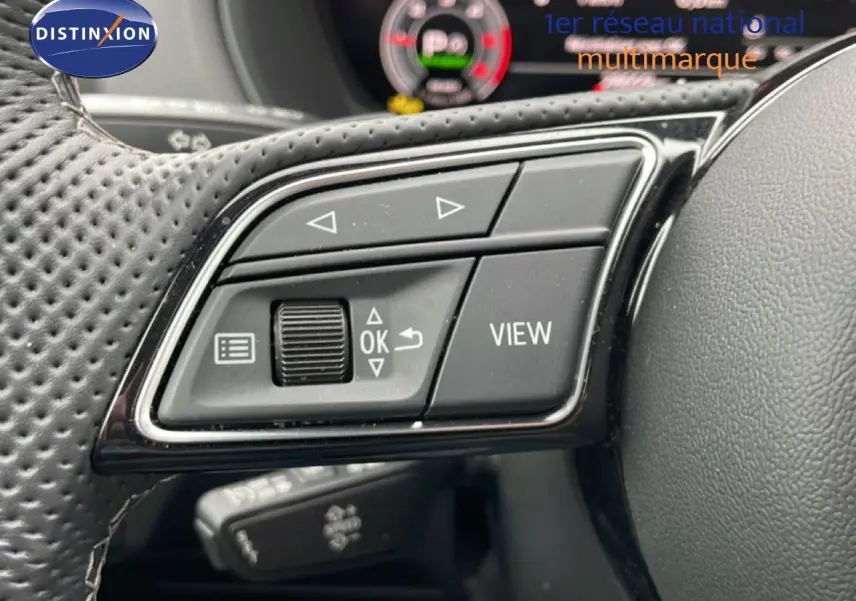 Gros plan sur les commandes gauche du volant en cuir perforé d’un Audi Q2 argent rose, avec affichage numérique en arrière-plan.