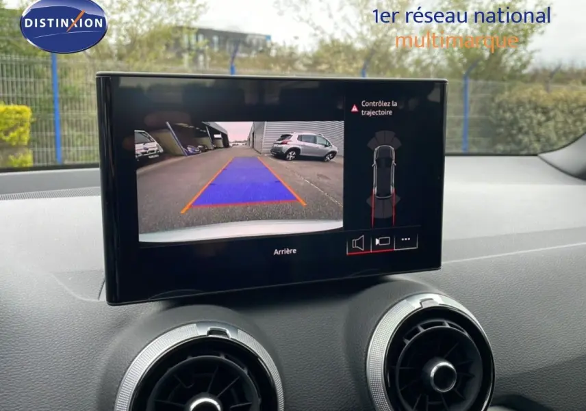 Écran central montrant la caméra de recul d’un Audi Q2 argent rose, avec vue arrière et guidage de trajectoire.