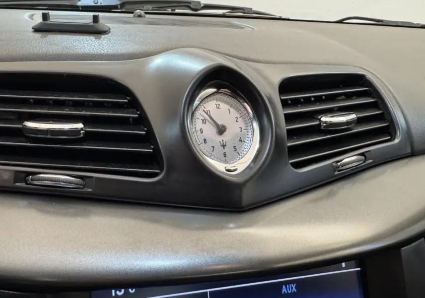 Gros plan sur l'horloge centrale et les aérateurs noirs du tableau de bord gris foncé de la Maserati Granturismo S 4.7.