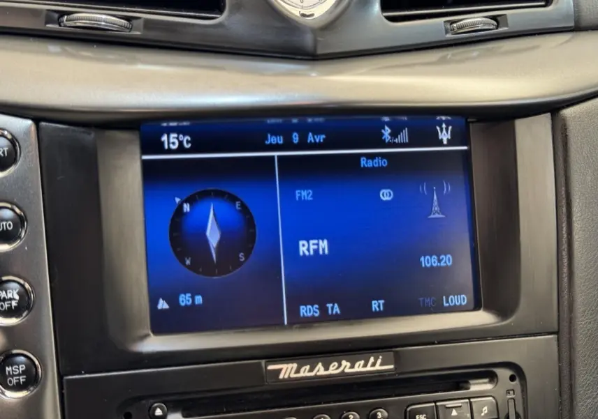 Gros plan sur l’écran central bleu du système multimédia de la Maserati Granturismo S 4.7, avec horloge et logo Maserati.