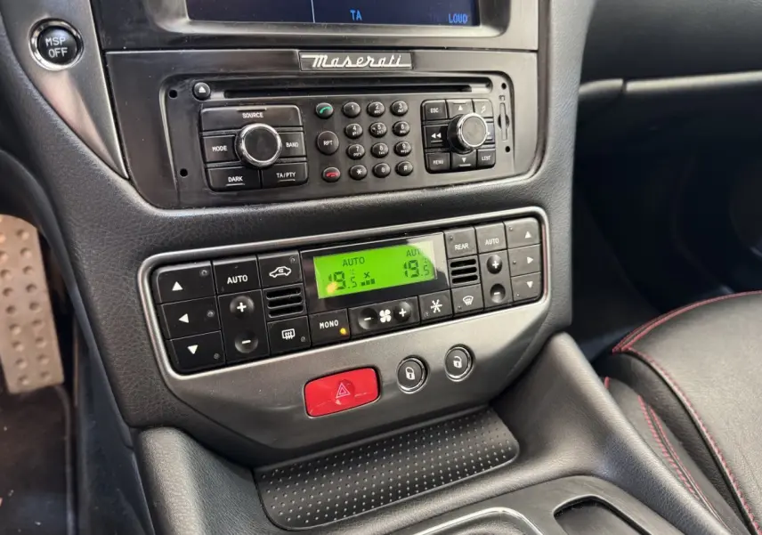 Vue rapprochée de la console centrale noire de la Maserati Granturismo S 4.7 2010 avec commandes climatisation et radio.
