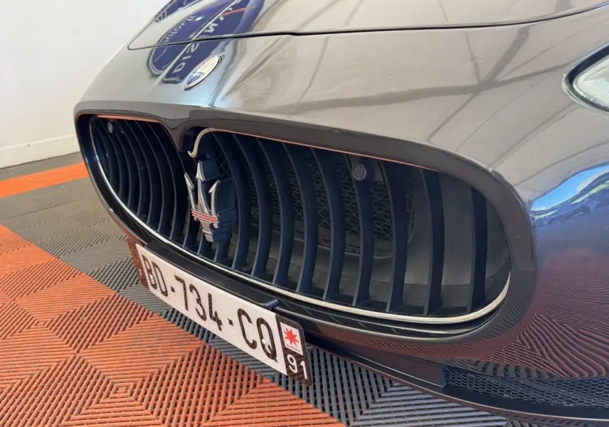 Gros plan sur la calandre avant gris foncé de la Maserati Granturismo S 4.7 avec logo trident et plaque d'immatriculation.