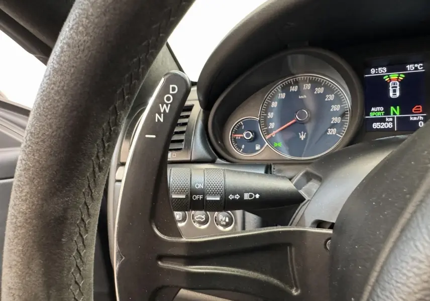 Gros plan sur le volant et le compte-tours bleu de la Maserati Granturismo S 4.7 gris foncé, avec palette de vitesse "DOWN".