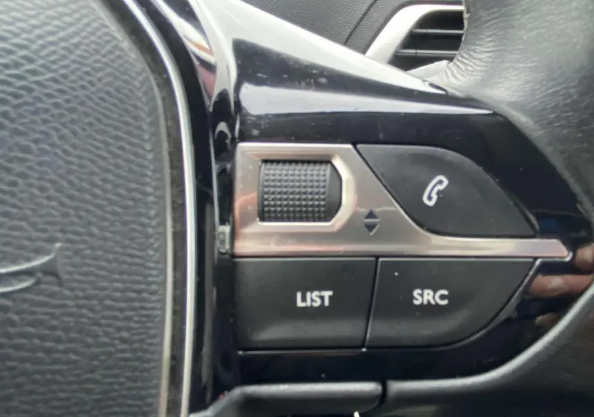 Gros plan sur les commandes du volant noir du Peugeot 3008, boutons LIST et SRC visibles.