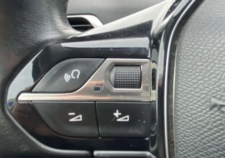 Gros plan sur les commandes de volume au volant du Peugeot 3008, finition noire brillante et cuir texturé.