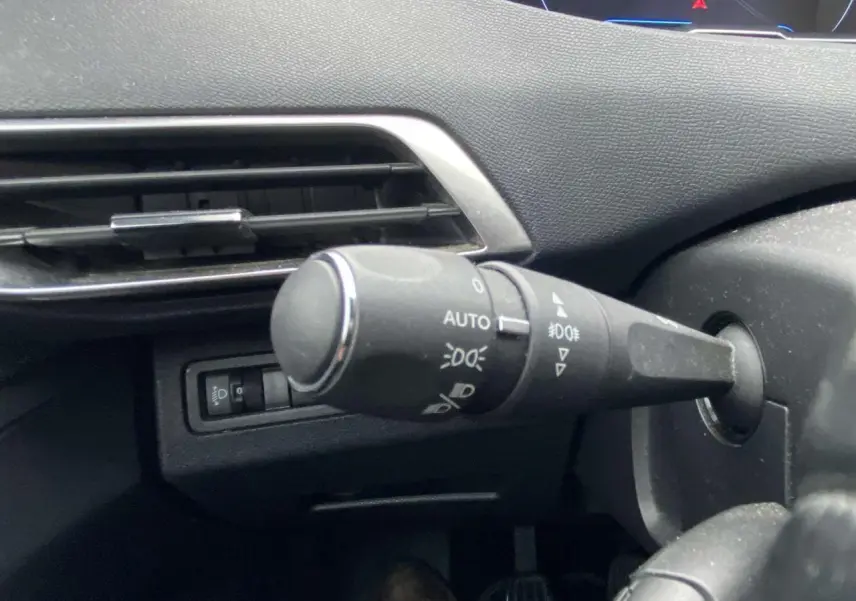Gros plan sur la commande d’éclairage à gauche du volant dans l’habitacle du Peugeot 3008 marron foncé.