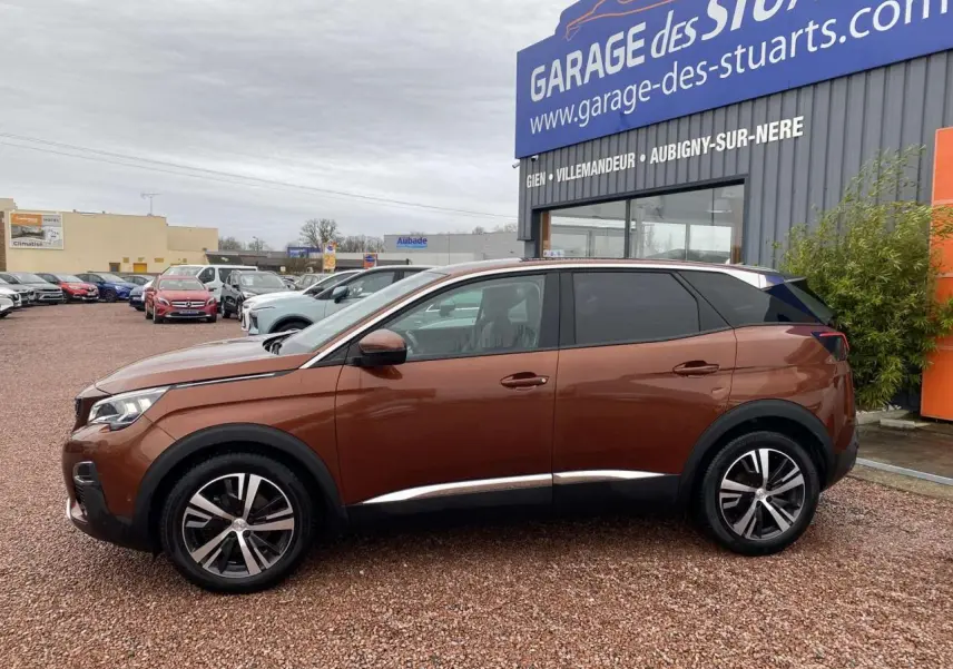 Vue de profil côté gauche d’un Peugeot 3008 marron foncé avec jantes alliage 18 pouces, stationné devant un garage.