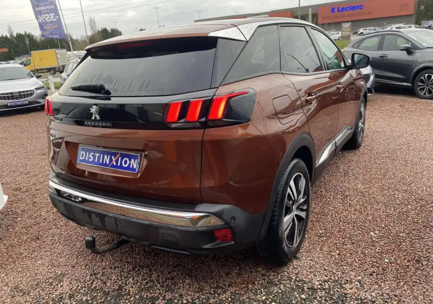 Vue 3/4 arrière droite d'un Peugeot 3008 marron foncé avec attelage et jantes alliage 18 pouces sur parking.