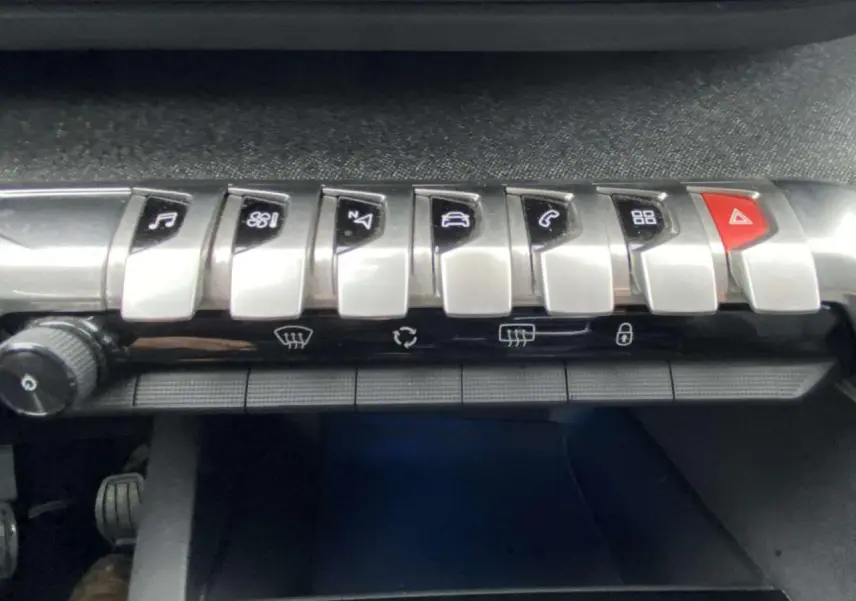 Gros plan sur la rangée de boutons de commande argentés et rouge du tableau de bord du Peugeot 3008 marron foncé.