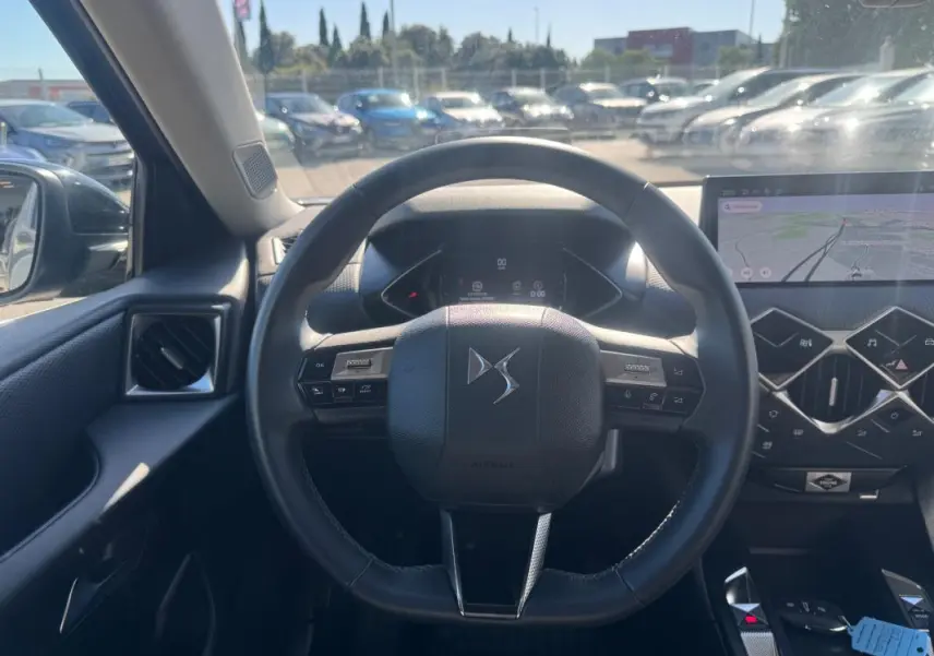 Vue intérieure centrée sur le volant DS d’une DS3 2024, avec tableau de bord numérique et écran tactile de navigation.