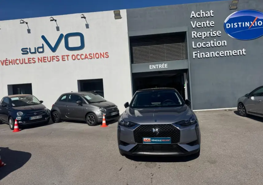 Vue de face d'une DS3 100 BVM6 Bastille gris avec calandre distinctive et jantes alliage 18 pouces, stationnée devant un garage.