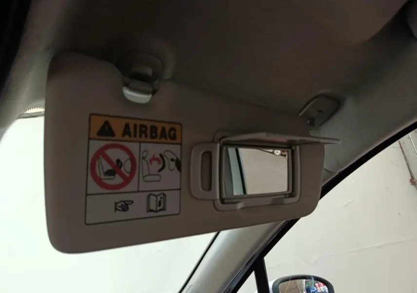 Détail intérieur du pare-soleil côté conducteur avec miroir et avertissement airbag dans une Renault Clio blanche.