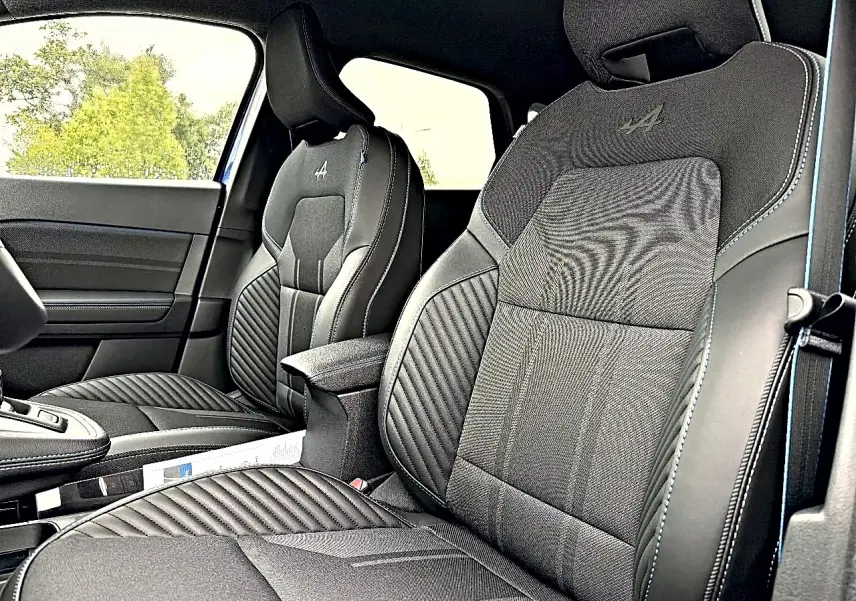 Vue intérieure des sièges avant noirs avec surpiqûres bleues et logo Alpine brodé sur les appuie-têtes du Renault Symbioz 2026.