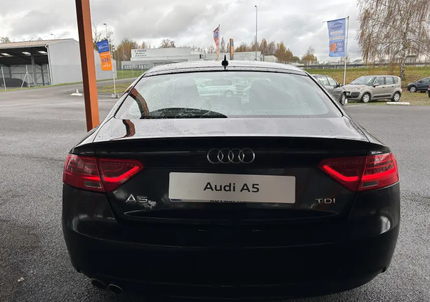 Vue arrière d'une Audi A5 Sportback noire de 2013 avec feux arrière allumés et double sortie d'échappement visible.