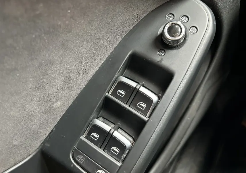 Gros plan sur les commandes de lève-vitres et réglage des rétroviseurs côté conducteur d'une Audi A5 Sportback noire de 2013.