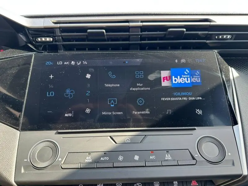 Vue rapprochée de l’écran tactile central noir du tableau de bord de la Peugeot 308 bleu, affichant les commandes multimédia et climatisation.