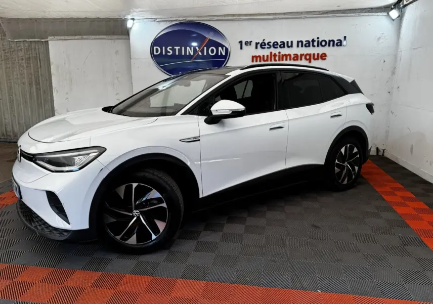 Volkswagen ID.4 blanc en 3/4 avant droit, avec jantes noires et toit panoramique dans un showroom.