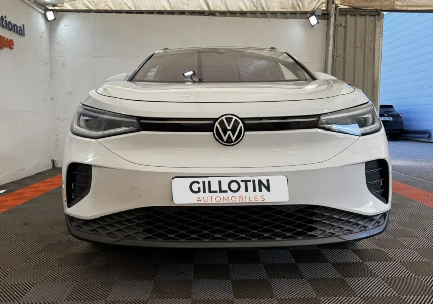 Vue frontale d’un Volkswagen ID.4 blanc avec calandre noire et logo VW centré, en intérieur showroom.