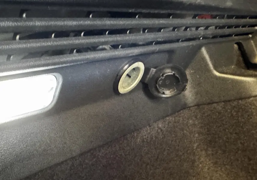 Détail intérieur du coffre du Volkswagen ID.4 77 kWh blanc montrant la prise 12V et l’éclairage d’ambiance.