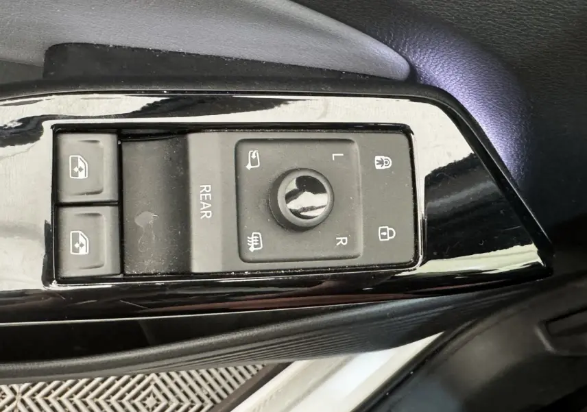 Gros plan sur les commandes noires de réglage des rétroviseurs et des vitres côté conducteur d’un Volkswagen ID.4 blanc.
