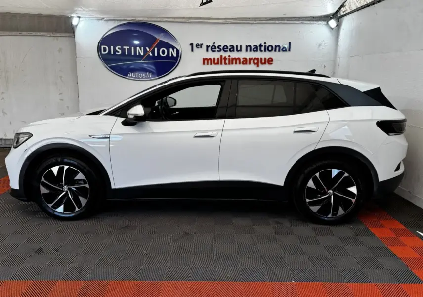 Vue de profil côté gauche d'un Volkswagen ID.4 blanc avec jantes noires et toit noir dans un showroom.