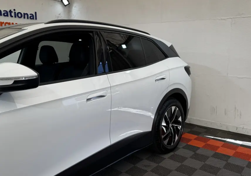 Vue côté droit arrière du Volkswagen ID.4 blanc avec jantes noires et vitres teintées en intérieur showroom.