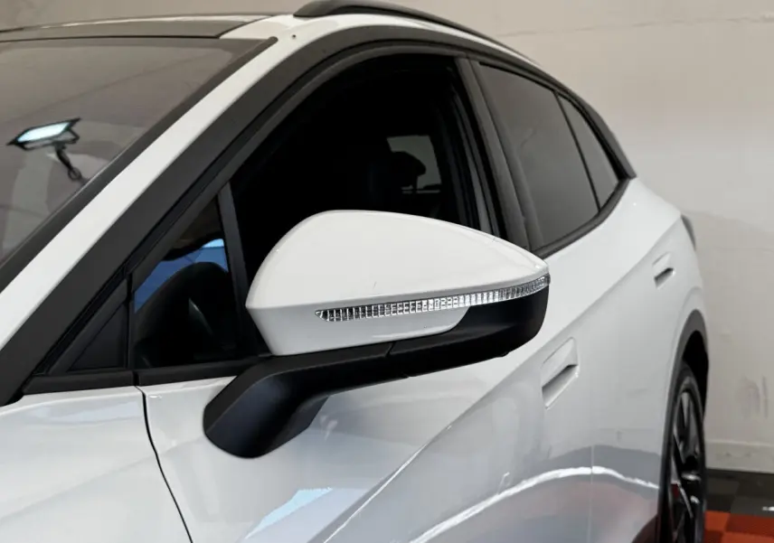 Vue latérale côté gauche d'un Volkswagen ID.4 blanc, mettant en valeur le rétroviseur rabattable avec clignotant intégré.